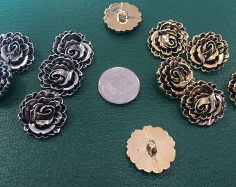 May include: Assortment of gold and silver metal buttons with a rose design. The buttons are arranged on a green surface.