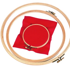 Op de afbeelding: Drie houten borduurringen van verschillende maten, met een felrood stuk stof gespannen over de kleinste ring. De ringen zijn gemaakt van lichtgekleurd hout en hebben messingkleurige spanmechanismen. De stof heeft een rasterpatroon.