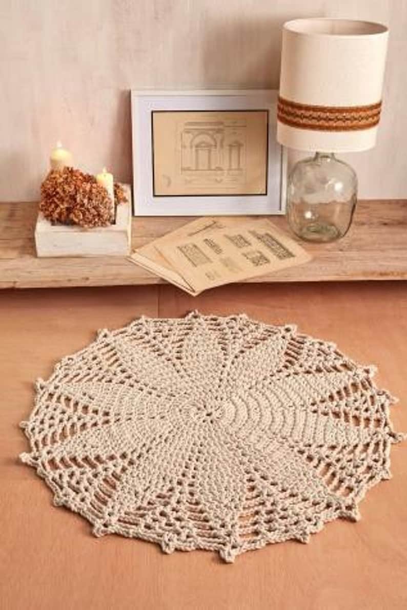 May include: A large, round, crocheted rug in a cream color with a delicate, intricate pattern. The rug is made of thick yarn and has a soft, textured surface.
