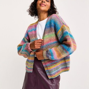 May include: A vibrant, striped cardigan in shades of blue, pink, yellow, and green. The open-front sweater has long sleeves and a relaxed fit. The model is wearing a white top and a burgundy leather skirt.