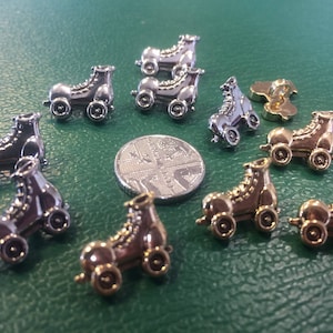 May include: Assortment of silver and gold roller skate charm buttons. The buttons are in the shape of a roller skate with a single wheel on each side.