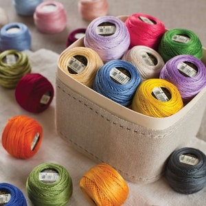 May include: A basket filled with colorful embroidery floss spools in various shades of blue, green, red, yellow, purple, and white. The spools are arranged in a circular pattern and are ready for crafting projects.