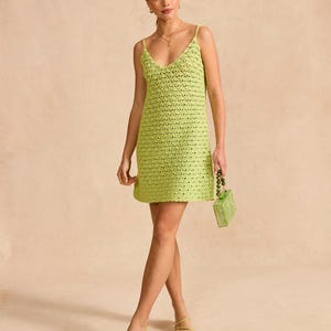 Può includere: Un mini abito in crochet verde lime con scollo a V e spalline sottili. L'abito è realizzato in un tessuto leggero e traspirante e ha una vestibilità rilassata. La modella indossa l'abito con un paio di sandali con tacco verde lime e una borsa a tracolla con perline verde lime.