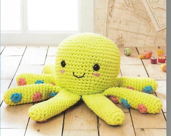 May include: A crocheted yellow octopus amigurumi toy with pink and blue accents. The toy is sitting on a wooden floor. The image includes the text "DMC Crochet Amigurumi" and the logo for NaturaXL Just Cotton Yummy Colors.