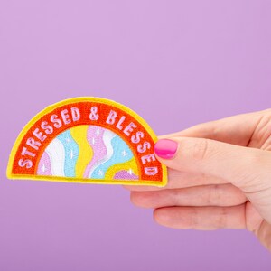 May include: A yellow, orange and pink embroidered patch with the text "Stressed & Blessed" in a rainbow arch design.