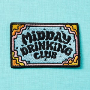 May include: Embroidered patch with the text "MIDDAY DRINKING CLUB" in black, stylized lettering. The patch has a light blue background with a decorative border in pink, yellow, and orange. The patch is rectangular with rounded corners.