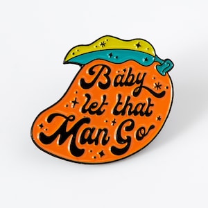 May include: Orange enamel pin shaped like a mango with the text "Baby let that Man Go" in black script.