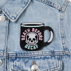 May include: An embroidered patch featuring a black coffee mug with the text "Death Before Decaf" in pink lettering. The mug has a white rim and handle.