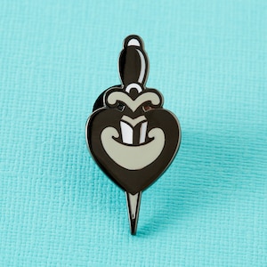 May include: Black enamel pin with a white dagger piercing a heart. The heart is outlined in black and has a white smile.