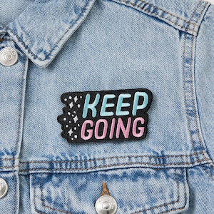 May include: A black denim jacket with a black embroidered patch that says "KEEP GOING" in pink and blue lettering with white stars.