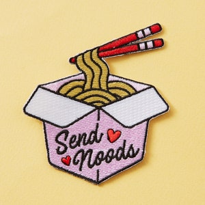 May include: A pink and white embroidered iron-on patch with a cartoon image of a takeout container filled with noodles and chopsticks. The text "Send Noods" is written in black with two red hearts.
