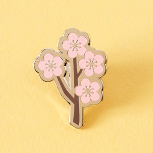 May include: A gold-toned enamel pin featuring a stylized pink cherry blossom tree with five blossoms.