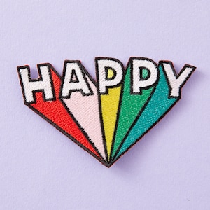 Pode incluir: Um remendo bordado colorido com a palavra "HAPPY" em letras brancas sobre um fundo arco-íris.