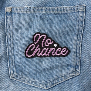 Op de afbeelding: Een roze en zwarte geborduurde patch met de tekst "No Chance" en een klein wit hartje.