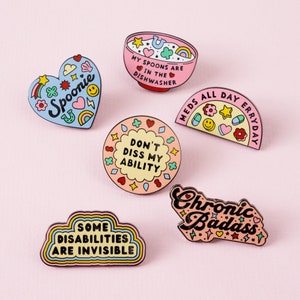 May include: Set of nine enamel pins with colorful designs and text. The pins feature phrases like "Spoonie", "Don't Diss My Ability", "Meds All Day Erryday", "Chronic Badass", and "Some Disabilities Are Invisible".