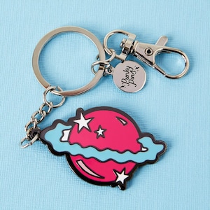 May include: A silver keychain with a pink and blue planet charm and a silver charm that says "Punk'y Pins".