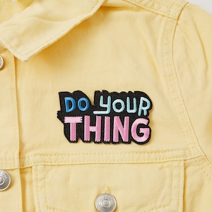 Puede incluir: Una chaqueta vaquera amarilla con un parche bordado en negro, rosa y azul que dice "Do your thing".