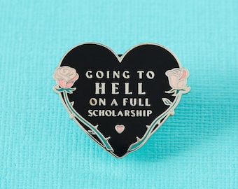 May include: Black heart-shaped enamel pin with a silver outline. The pin features a rose on each side and the text "Going to Hell on a Full Scholarship".