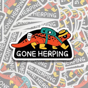 May include: A sticker depicting a cartoon lizard wearing a backpack, boots, and a hat, with the words "GONE HERPING" in white on a black background. The lizard is red with black spots and yellow details. The background is filled with similar stickers.