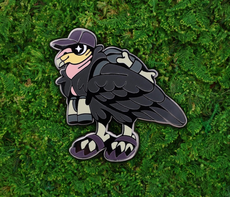 May include: A cartoon-style enamel pin of a vulture wearing a purple baseball cap and sunglasses. The vulture has black feathers, a pink neck, and is wearing a backpack and sandals. The pin is set against a green background.
