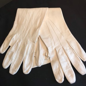 May include: A pair of white leather gloves. The gloves are folded in half and the fingers are extended.