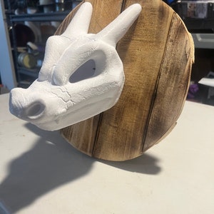 May include: White dragon head sculpture mounted on a wooden plaque. The dragon has a textured surface and a detailed face.
