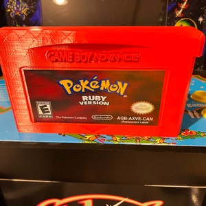 May include: A red Game Boy Advance game cartridge case with a Pokemon Ruby Version game cartridge inside. The case has a textured surface and the cartridge label features the Pokemon logo, the words "Pokemon Ruby Version", and the Nintendo logo.