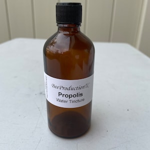 May include: A brown glass bottle with a black cap, labeled "BeeProduction'TC Propolis Water Tincture".