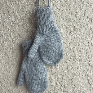 May include: A pair of gray knitted mittens with long ties hanging from a wall.