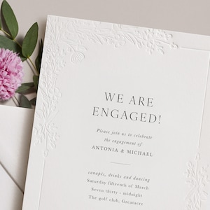 May include: A white rectangular engagement invitation card with embossed floral borders. The text reads: WE ARE ENGAGED! Please join us to celebrate the engagement of ANTONIA & MICHAEL, canapés, drinks and dancing, Saturday fifteenth of March.
