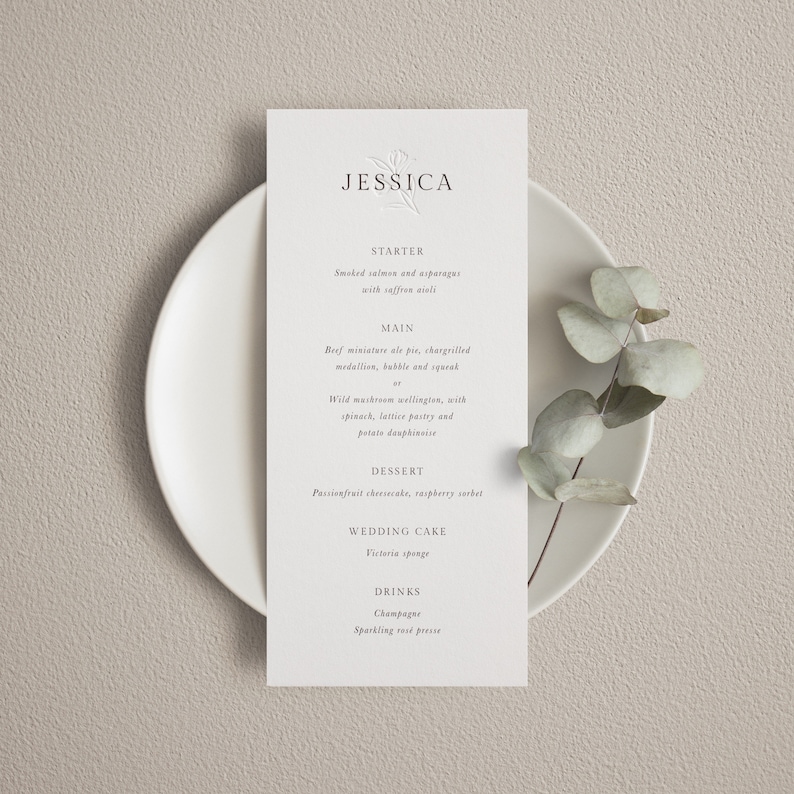 May include: A wedding menu card with a floral design and the name Jessica at the top. The menu includes starter, main, dessert, wedding cake, and drinks. The starter is smoked salmon and asparagus with saffron aioli. The main is beef miniature pie, chargrilled medallion, bubble and squeak, or wild mushroom wellington, with spinach, lattice pastry and potato dauphinoise. The dessert is passionfruit cheesecake, raspberry sorbet. The wedding cake is Victoria sponge. The drinks are champagne and sparkling fruit presse.