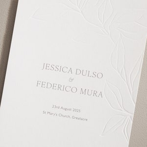 Puede incluir: Una invitación de boda blanca con un diseño floral sencillo. La invitación dice "Jessica Dulso & Federico Mura" e incluye la fecha "23 de agosto de 2025" y la ubicación "St Mary's Church, Greatacre".