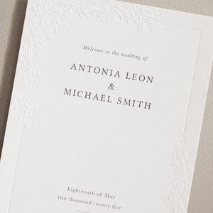 May include: Wedding invitation with a floral design border. The text reads "Welcome to the wedding of Antonia Leon & Michael Smith. Eighteenth of May, two thousand twenty five."