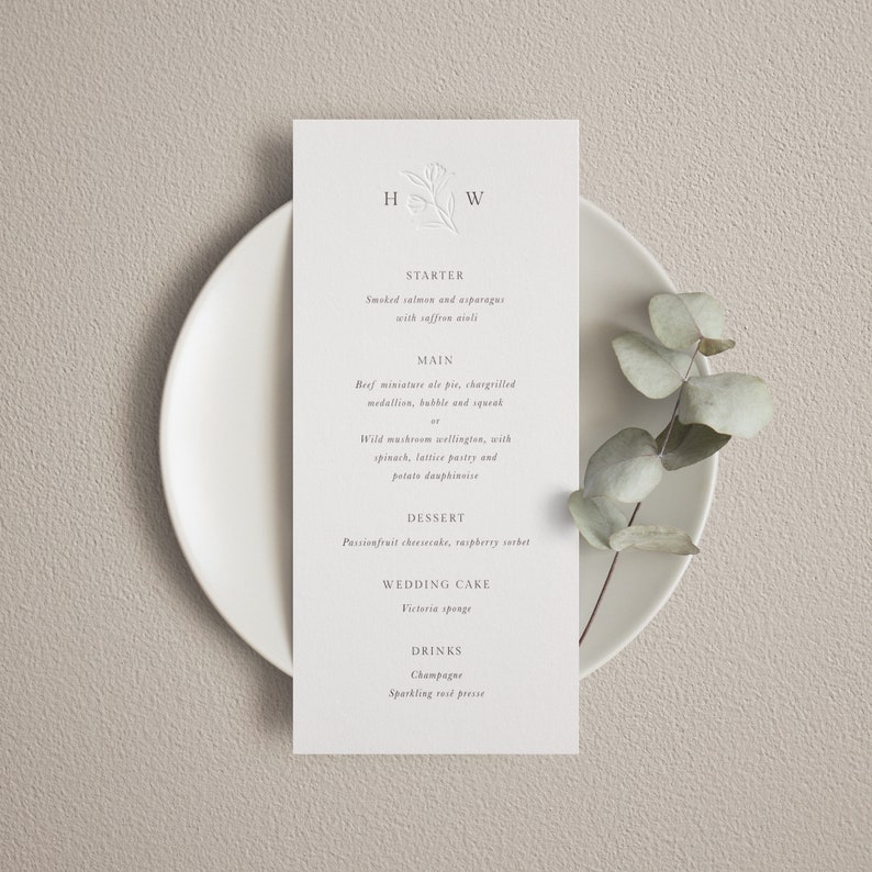 May include: A wedding menu card with a floral design at the top. The menu includes starter, main, dessert, wedding cake, and drinks. The menu items are: Smoked salmon and asparagus with saffron aioli, Beef miniature ale pie, chargrilled medallion, bubble and squeak, Wild mushroom wellington, with spinach, lattice pastry and potato dauphinoise, Passionfruit cheesecake, raspberry sorbet, Victoria sponge, Champagne, Sparkling rose presse.