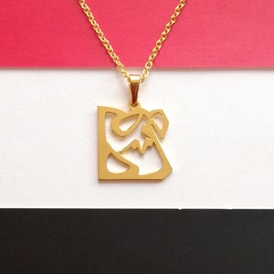 May include: A gold chain necklace with a pendant featuring a stylized Arabic calligraphy design. The pendant is a square shape with a cutout design.