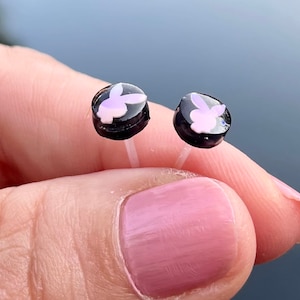 May include: A pair of small, black stud earrings with a pink bunny rabbit design.