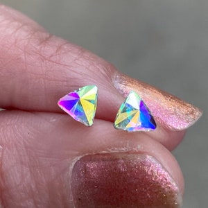 May include: A pair of iridescent triangle-shaped earrings. The earrings are small and have a subtle sparkle.