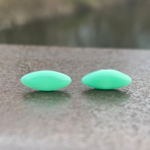 Pode incluir: Dois pequenos brincos ovais de cor verde claro.