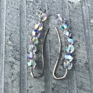 May include: A pair of silver earrings with a curved design. Each earring is adorned with a row of clear iridescent crystals.