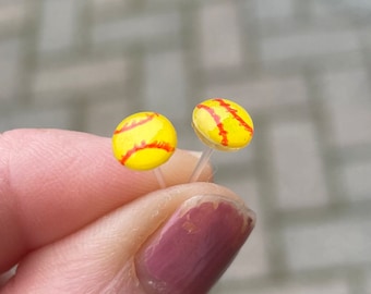 Op de afbeelding: Een paar kleine, gele en rode softbal-oorbellen. De oorbellen zijn op een doorzichtige post.