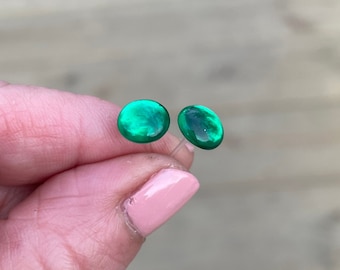 Op de afbeelding: Een paar ronde groene glazen oorbellen. De oorbellen worden in een hand gehouden.
