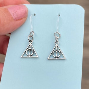 Könnte beinhalten: Ein Paar silberne Ohrringe mit einem dreieckigen Anhänger, der das Symbol der Heiligtümer des Todes aus der Harry-Potter-Reihe zeigt.