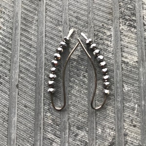 May include: A pair of silver hoop earrings with a row of small, faceted, black beads on each hoop.