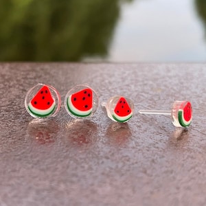 May include: Three pairs of watermelon slice stud earrings. The earrings are made of clear plastic with a red watermelon slice design.