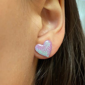 May include: A pair of iridescent purple heart-shaped earrings. The earrings are small and have a subtle shimmer.