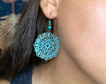 Op de afbeelding: Een paar turquoise blauwe oorbellen met een delicaat, ingewikkeld, cirkelvormig ontwerp. De oorbellen zijn gemaakt van metaal en hebben een hangende, kralenversierde druppel.