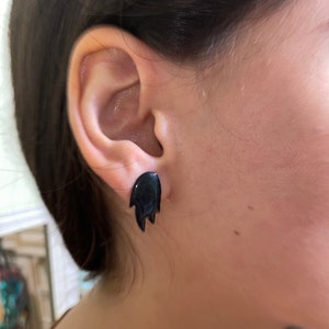 May include: A pair of black flame-shaped stud earrings. The earrings are small and delicate, and they are made of a smooth, shiny material.