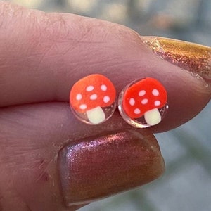 Könnte beinhalten: Ein Paar rote und weiße Pilz-Ohrstecker. Die Pilze haben weiße Punkte auf den roten Hüten.