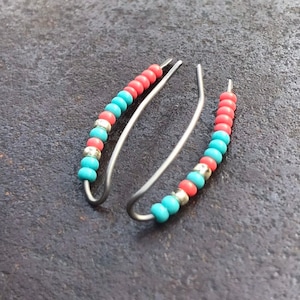 Op de afbeelding: Een paar zilveren creolen met turquoise en koraal gekleurde kralen.