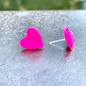 May include: A pair of pink heart-shaped stud earrings. The earrings are made of a shiny, smooth material.